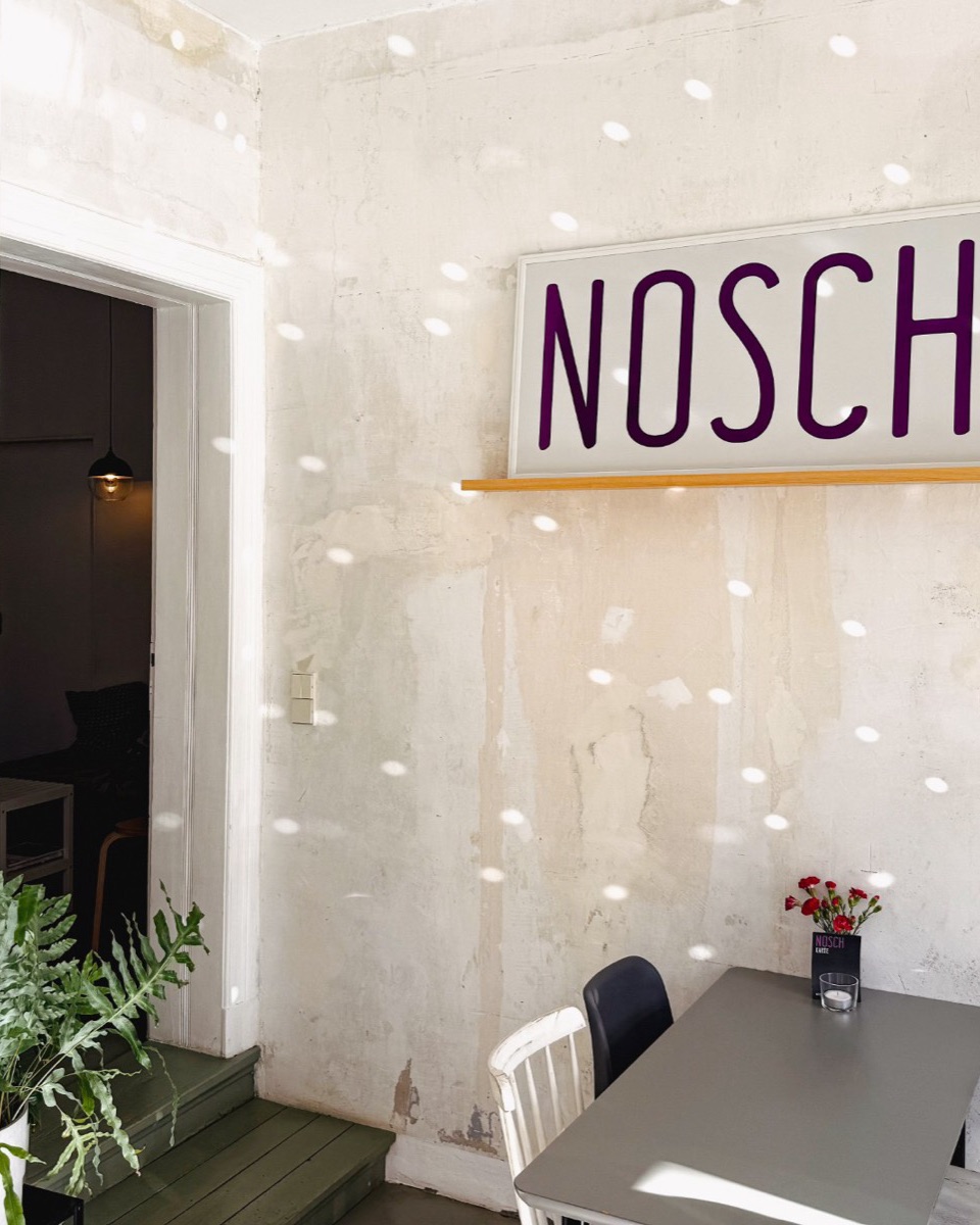 Gastraum des NOSCH mit Tischen, Blumen und dem NOSCH-Schild an der Wand