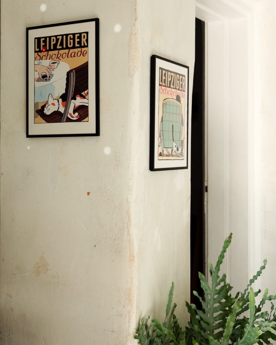 Zwei gerahmte Poster „Leipziger Schokolade“ von Janta Island an einer hellen Wand im NOSCH, davor eine Pflanze