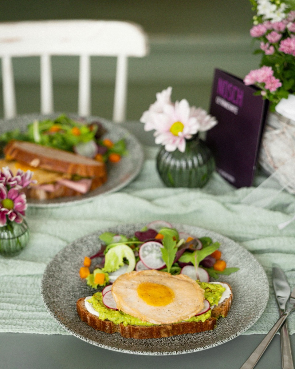 Stramme Rosa: veganes Spiegelei von Not Egg auf Brot mit Frischkäse, Avocado und Radieschen, daneben Salat und Blumen auf dem Tisch im NOSCH